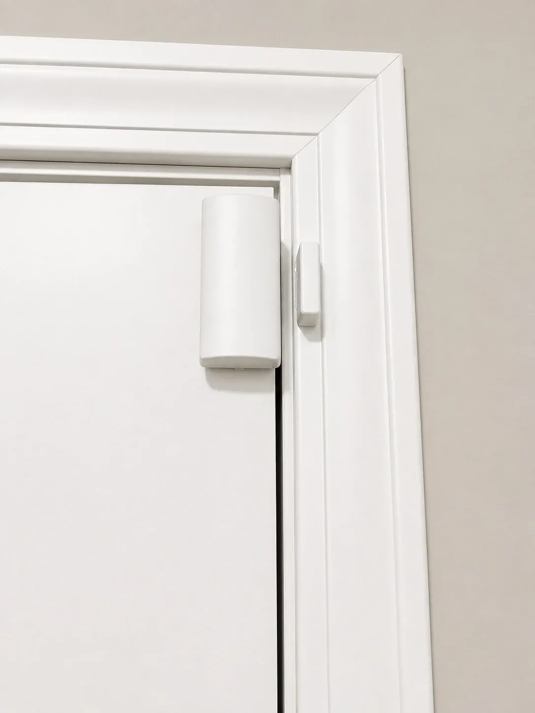 Surface-mounted door sensor: a white plastic housing on the face of the door with a matching magnet on the frame.